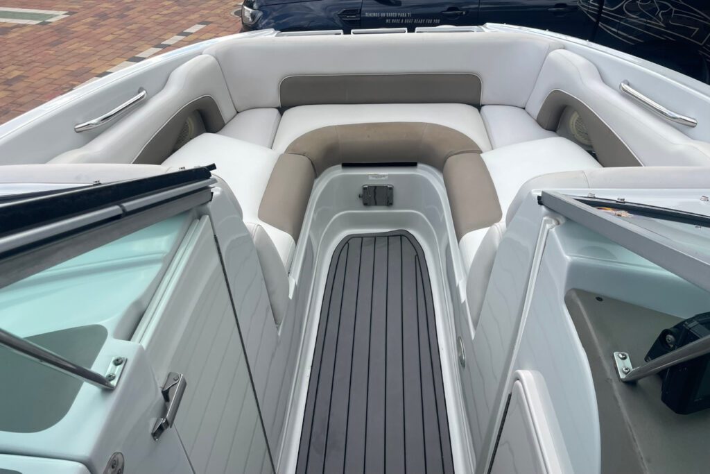 Interior de proa del bote Sea Ray E2XS con asientos blancos en U, piso de teca gris y puertas laterales de acceso